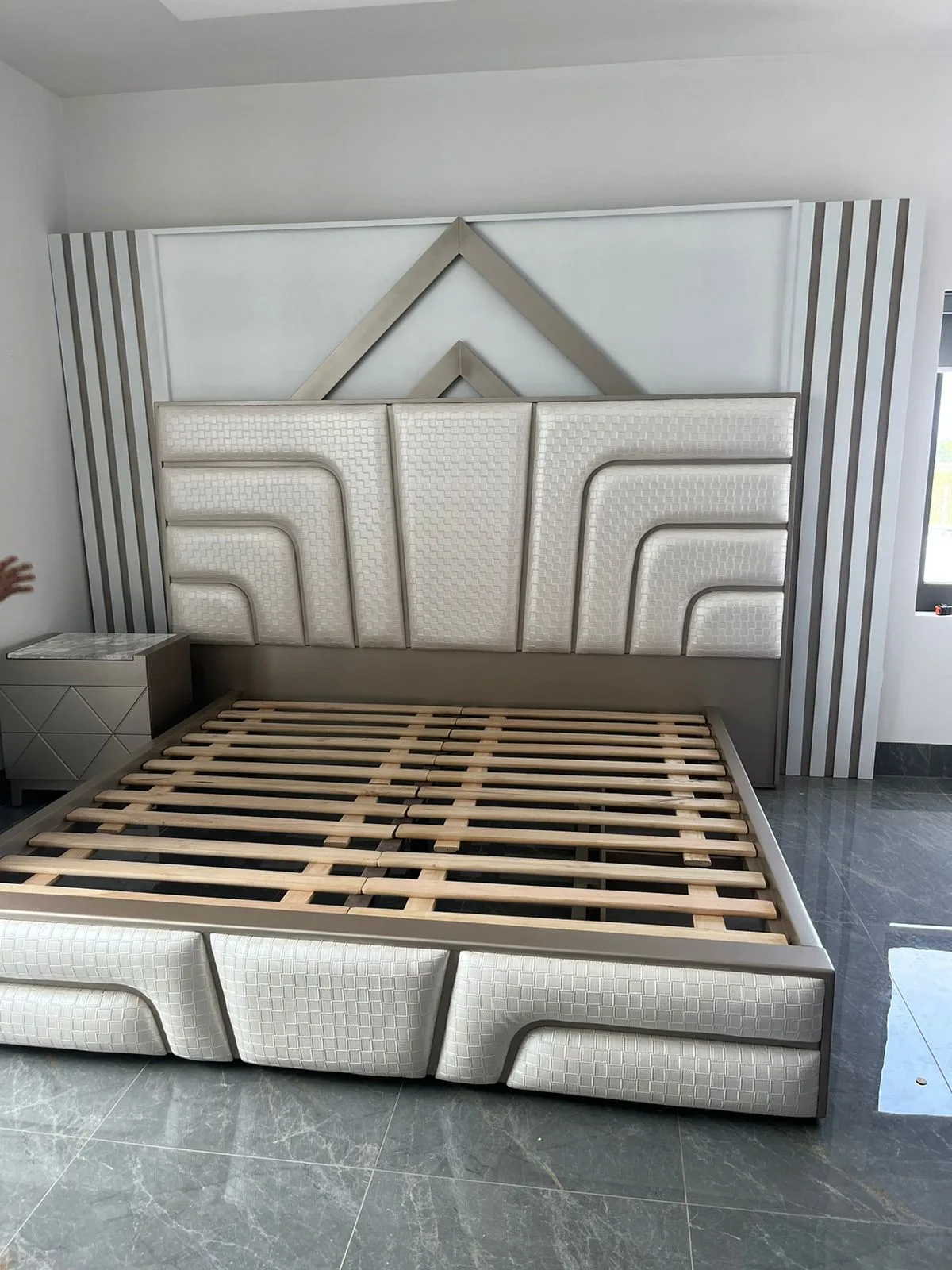 Cabecera de cama con textura tejida en canales curvos y remate metálico triangular (estilo art-decó)